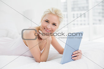 Smiling casual young blond with tablet PC in bed