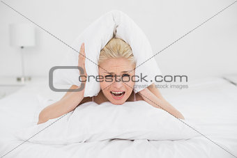 Angry woman covering ears with pillow in bed