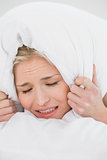 Displeased woman covering ears with pillow