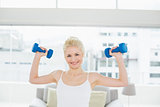 Smiling woman lifting dumbbells at fitness studio