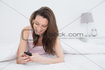Happy woman looking at mobile phone in bed