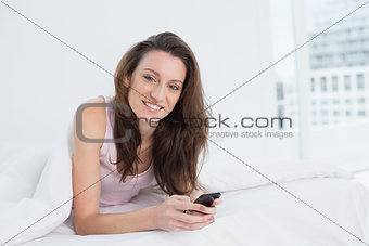 Happy young woman with mobile phone lying in bed