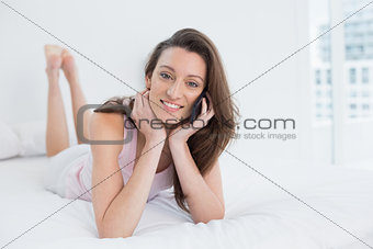 Smiling young woman using mobile phone in bed