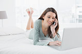 Casual woman using cellphone and laptop in bed