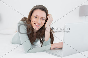 Cheerful relaxed casual young woman with laptop in bed