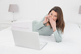 Shocked casual woman using cellphone and laptop in bed