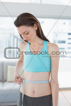 Toned woman measuring waist in fitness studio