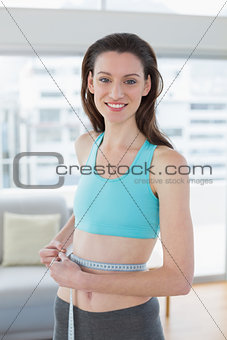 Toned woman in sportswear measuring waist in fitness studio