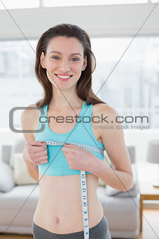 Smiling woman in sportswear measuring chest in fitness studio