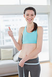 Toned woman measuring waist while gesturing thumbs up
