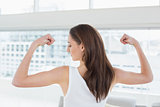 Fit brown haired woman flexing muscles in fitness studio