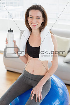 Woman sitting on exercise ball with water bottle in fitness studio