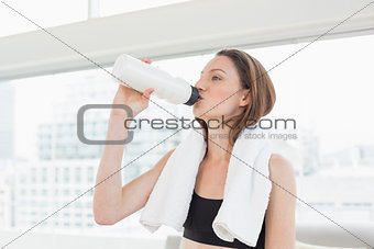 Woman with towel around neck drinking water in fitness studio