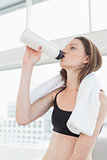 Fit woman with towel around neck drinking water in fitness studio