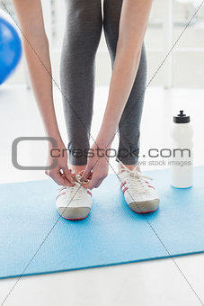 Low section of woman tying shoes with water bottle on floor