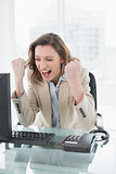 Businesswoman cheering with clenched fists at office desk