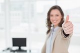 Elegant smiling businesswoman gesturing thumbs up in office