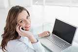 Brown haired businesswoman using laptop and cellphone in office