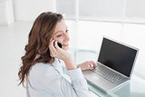 Businesswoman using laptop and cellphone in office