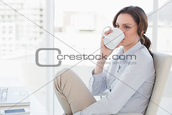 Businesswoman with laptop drinking coffee in office