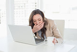 Sleepy businesswoman yawning in front of laptop at office