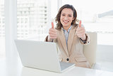 Smiling businesswoman gesturing thumbs up with laptop in office
