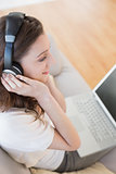 Woman using laptop while enjoying music on sofa in house