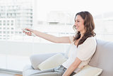 Smiling woman with remote control sitting on sofa