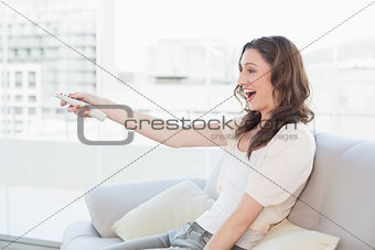 Cheerful young woman with remote control sitting on sofa