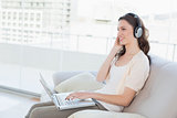 Casual woman using laptop while enjoying music on sofa