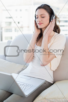 Relaxed woman with laptop enjoying music on sofa