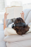 Brown haired woman enjoying music while reading book