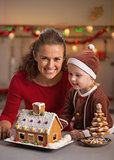 Portrait of happy mother and baby making christmas cookie house 