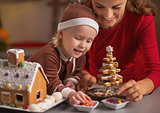 Happy mother and baby making christmas cookie house in kitchen