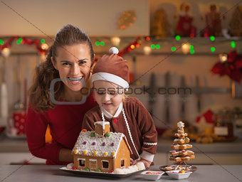 Smiling mother and baby decorating christmas cookie house in kit