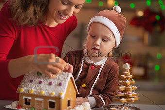 Happy mother and baby decorating christmas cookie house in kitch