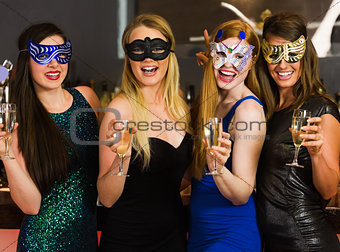 Laughing friends wearing masks holding champagne glasses