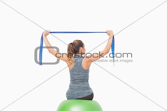 Blonde woman sitting on a fitness ball training with a resistance band