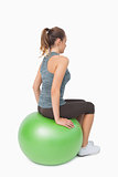 Side view of ponytailed woman sitting on fitness ball