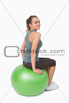 Young woman sitting on fitness ball looking over shoulder at camera