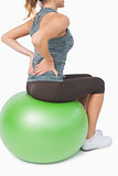 Mid section of young woman touching her back sitting on exercise ball