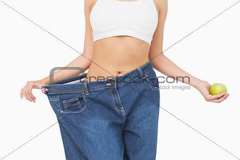 Mid section of slim woman wearing too big jeans holding an apple
