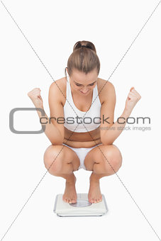 Successful young woman crouching on a scales