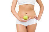 Young slim woman wearing a sports bra holding a green apple