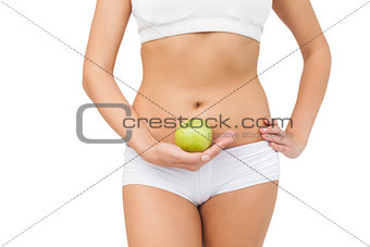 Young slim woman wearing a sports bra holding a green apple