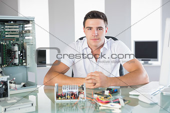 Handsome computer engineer sitting at desk looking at camera