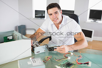 Attractive smiling computer engineer sitting at desk holding hardware