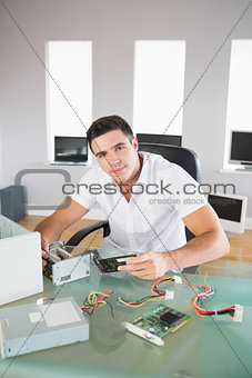 Attractive computer engineer sitting at desk holding hardware