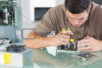 Handsome frowning computer engineer repairing hardware with pliers