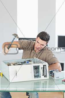 Handsome angry computer engineer destroying computer with hammer